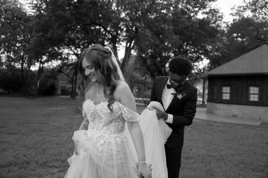 groom carrying the train of bride's wedding dress at Cross Creek Ranch wedding venue in Dallas, TX