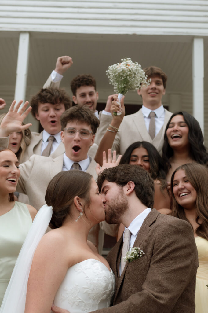 bride and groom kissing with wedding party cheering behind them by Dallas wedding photographer