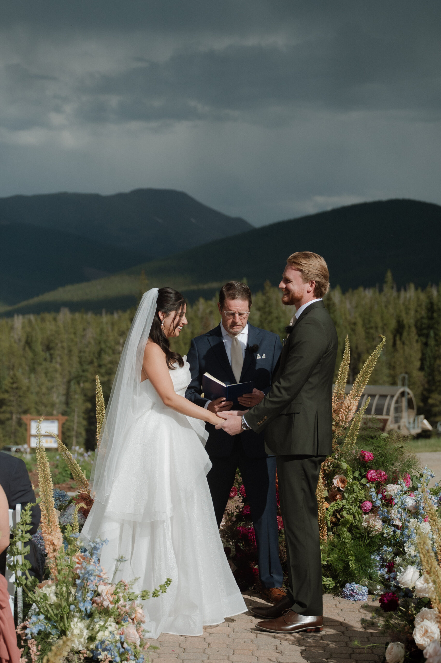 Outdoor wedding ceremony at TenMile Station with mountain views, bride and groom exchanging vows under dramatic Colorado skies in Breckenridge.