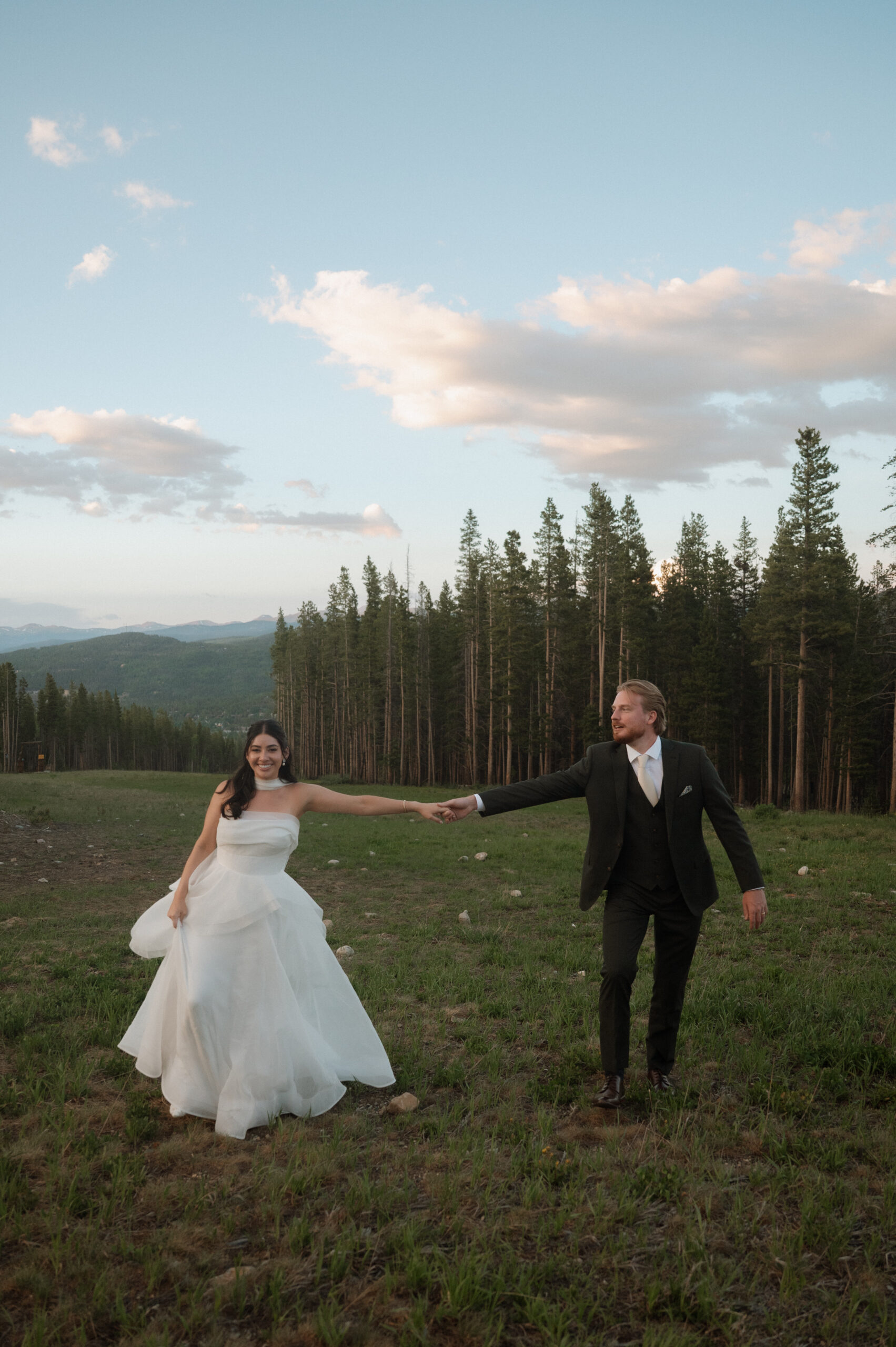Bride and groom walk hand-in-hand through a mountain meadow at TenMile Station during their summer wedding in Breckenridge, Colorado.
