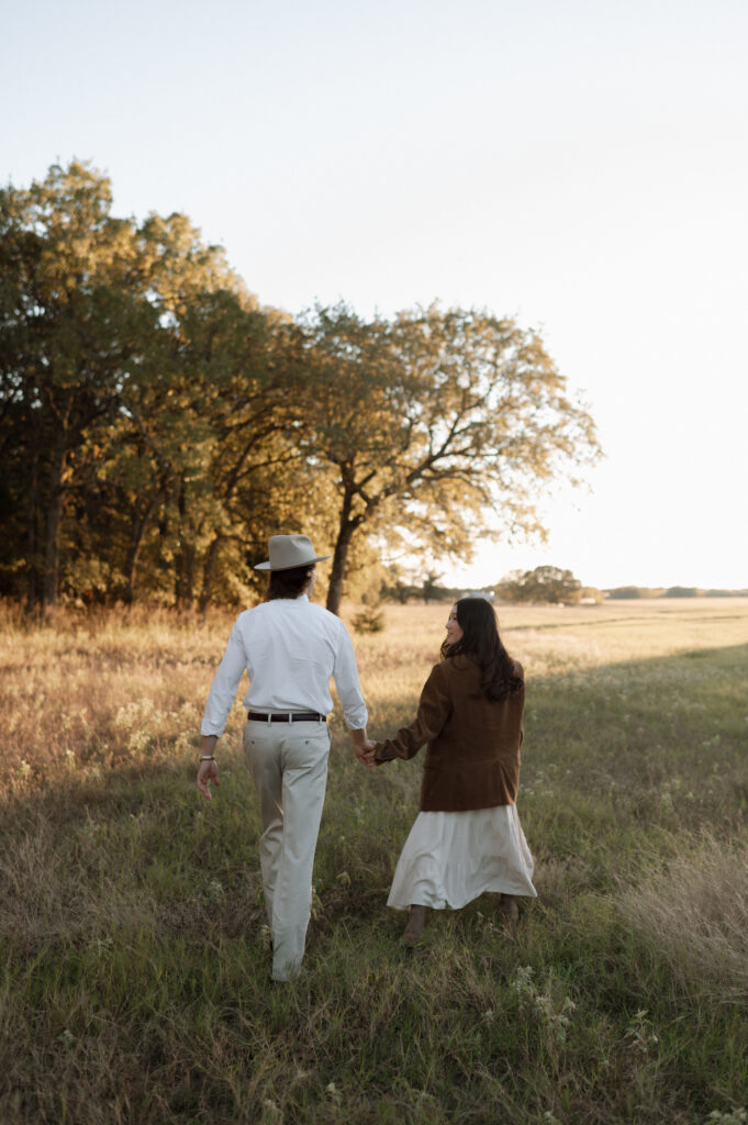 couple walking through a field at sunset