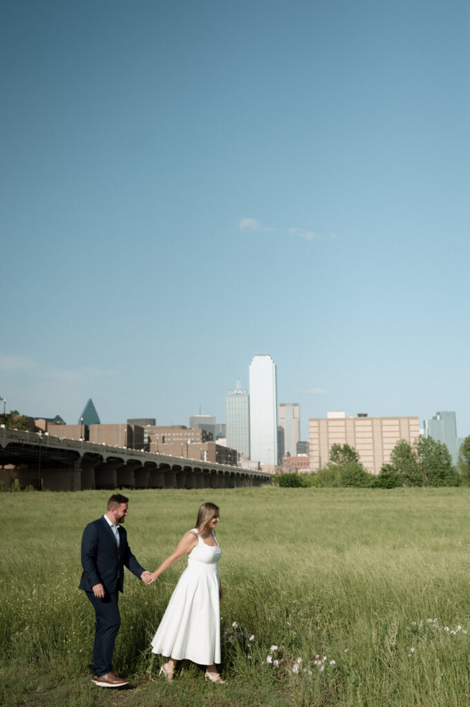 couple walking in a field with the Dallas Skyline behind them