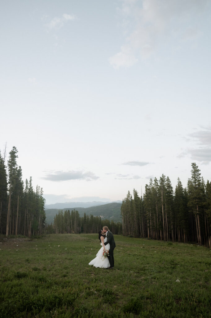 bride and groom kissing in a field in the mountains